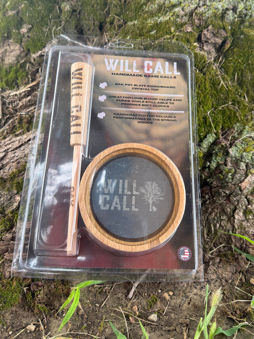Packaged Will Call handmade game calls set, including a wooden call and a round black-and-wood holder, displayed on a mossy tree trunk outdoors.